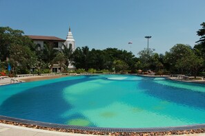 A large swimming pool with a tiled edge, surrounded by palm trees and a building with a pointed roof. - View Talay 3 Beach Apartments (Pattaya)