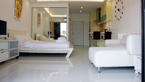 A modern hotel room with a bed, a sofa, a TV, and a bathroom visible through a glass door. - View Talay 3 Beach Apartments (Pattaya)