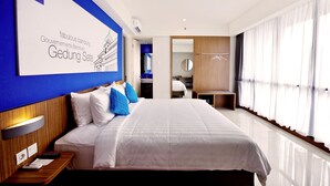 Ein modernes Hotelzimmer mit einem großen Bett, einem Nachttisch, einem Schreibtisch und einem im Hintergrund sichtbaren Badezimmer.