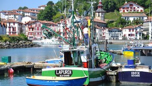 A harbor with boats named LAPURDI and IDFIX, surrounded by buildings with red roofs. - Boutique Hôtel Txoko (Saint-Jean-de-Luz)