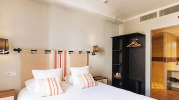 A neatly arranged hotel room with a large bed, a bedside table, a wardrobe, and a bathroom visible through an open door.