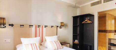 A neatly arranged hotel room with a large bed, a bedside table, a wardrobe, and a bathroom visible through an open door.