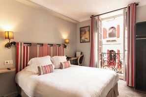 Une chambre d’hôtel avec un grand lit, deux lampes de chevet, un bureau et une vue sur un balcon avec des rideaux rouges.