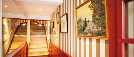 A hallway with striped wallpaper, a staircase, and framed artwork on the walls.