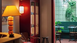 A cozy room with a bookshelf, a lamp, and a view of a green outdoor area. - Boutique Hôtel Txoko (Saint-Jean-de-Luz)