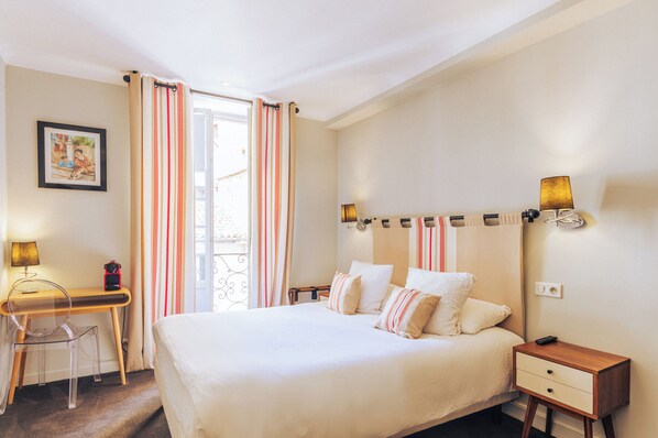 Une chambre d’hôtel comprenant un lit, une table de chevet, une lampe, un bureau, une chaise et des rideaux.