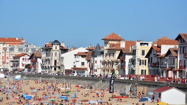 A beach with people sunbathing and swimming, and buildings with red-tiled roofs in the background. - Boutique Hôtel Txoko (Saint-Jean-de-Luz)