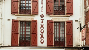 A building with multiple windows, each with red shutters and decorative ironwork. The name "HOTEL TXOKO" is prominently displayed on the facade. - Boutique Hôtel Txoko (Saint-Jean-de-Luz)