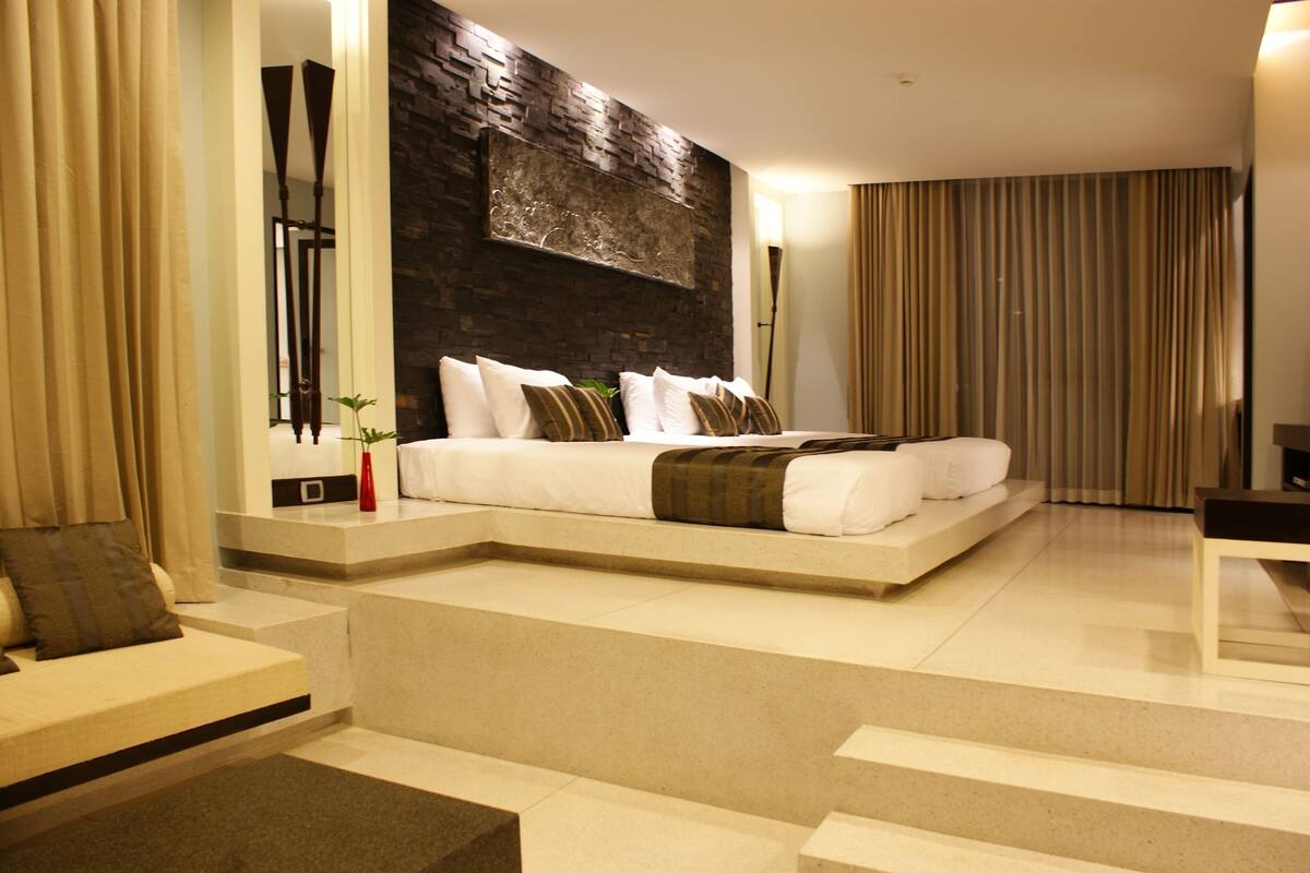 A modern bedroom with a large bed, a stone accent wall, and a view of the city.