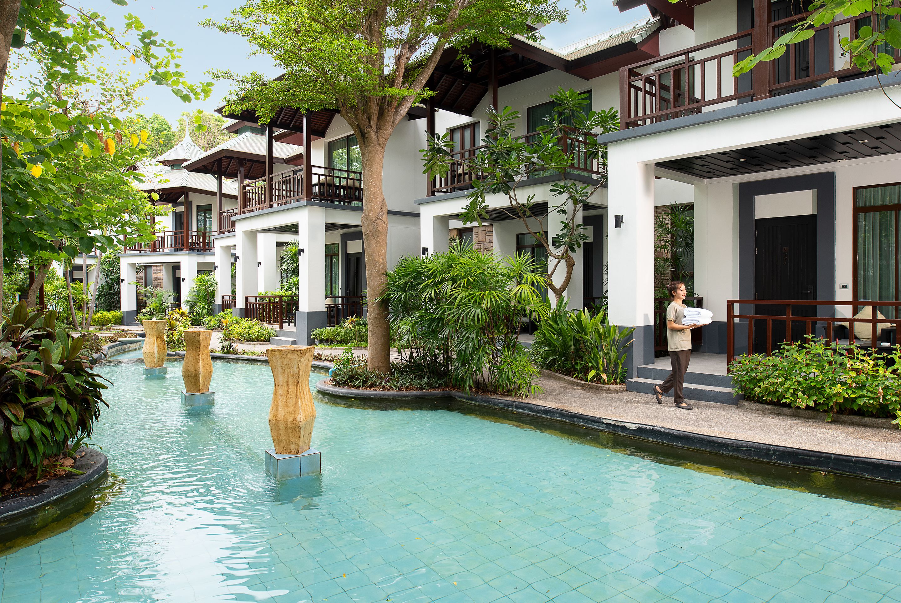 A hotel courtyard with a swimming pool, surrounded by lush greenery and multiple-story buildings with balconies.