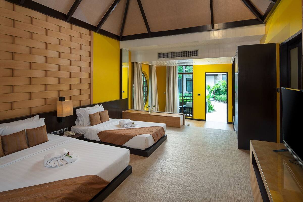 A hotel room with two beds, a TV, and a balcony with plants.