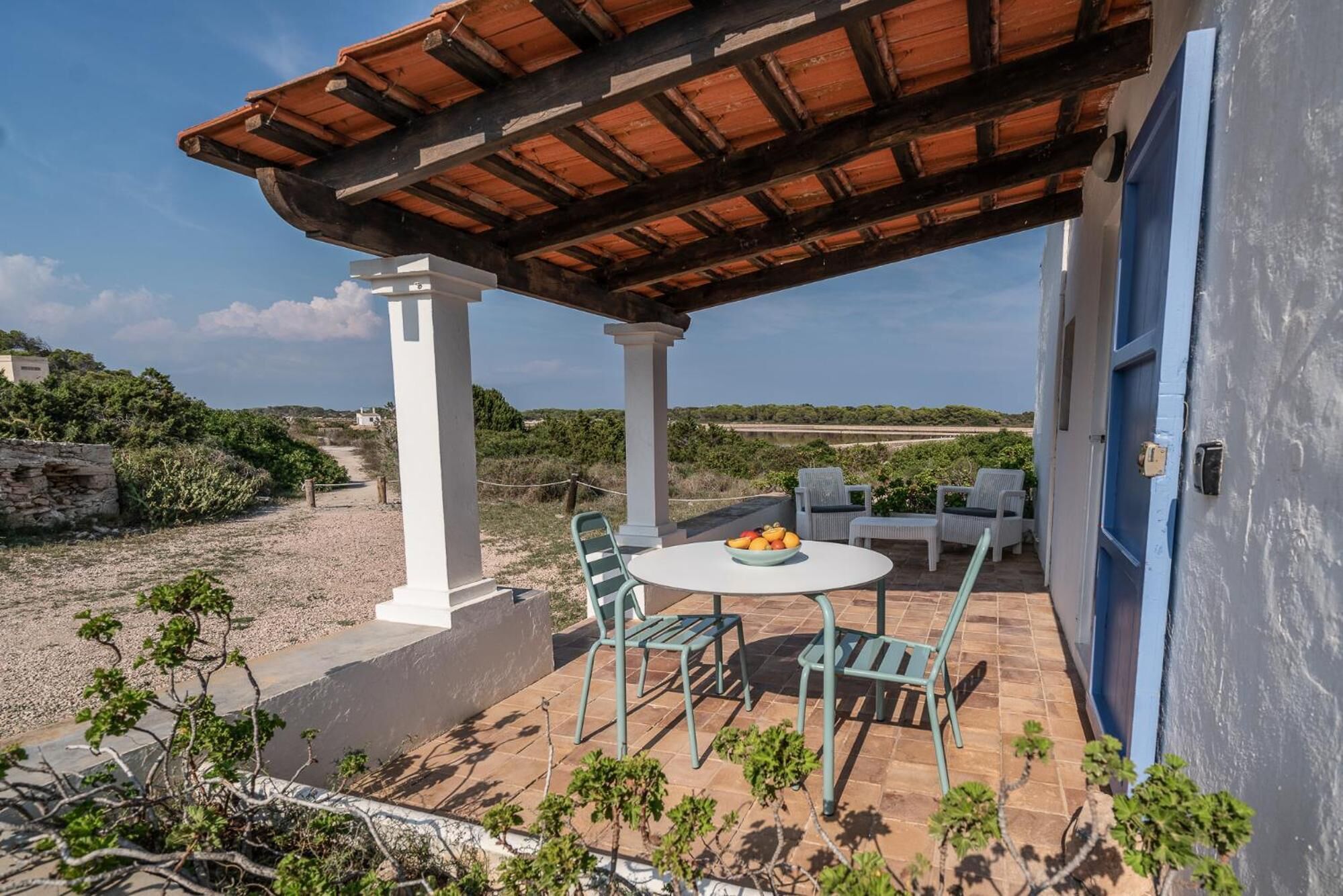 Un espacio de estar al aire libre cubierto con una mesa, sillas, un frutero y vistas del paisaje circundante.