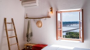 Une chambre avec une échelle en bois, un chapeau suspendu, une serviette et une fenêtre donnant sur un pont et l’eau.