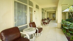 A corridor with wicker chairs and tables, large windows, and a tiled floor. - Hotel GRAND ROSELA Yogyakarta (Yogyakarta)