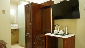 A compact room with a wooden wardrobe, a small table with a tray of items, a television mounted on the wall, and a bathroom with a sink and toilet visible. - Hotel GRAND ROSELA Yogyakarta (Yogyakarta)