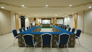 A conference room with a long table, chairs, a podium, and a projector screen. - Hotel GRAND ROSELA Yogyakarta (Yogyakarta)