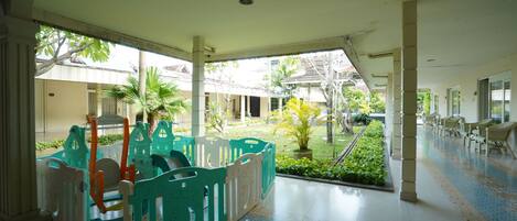 A hotel corridor with a play area featuring colorful plastic play structures and a view of the outdoor garden.
