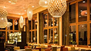 Un restaurant doté de nombreuses tables et chaises, de grandes fenêtres et de luminaires suspendus.