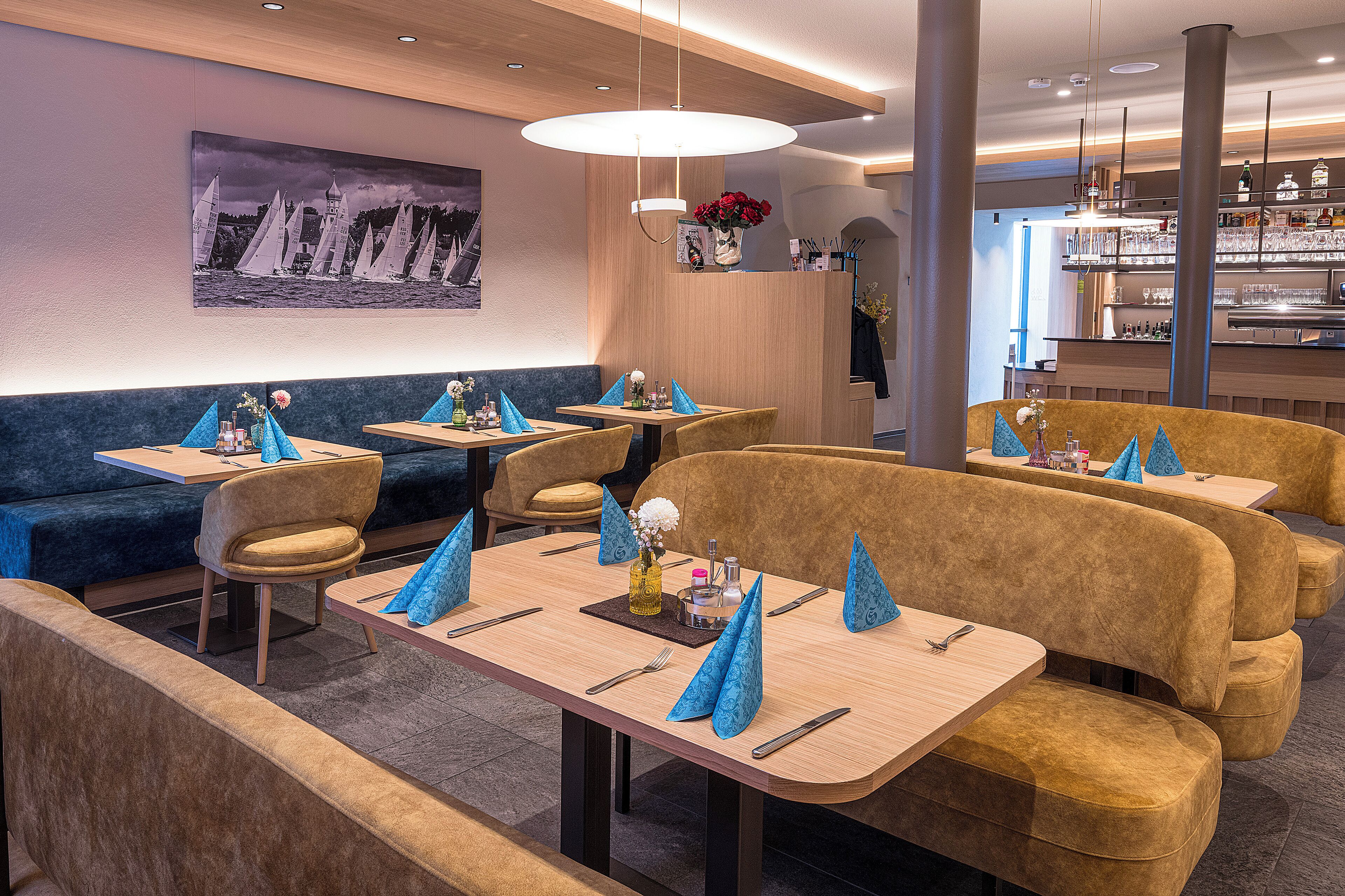 A restaurant with multiple tables and booths, a bar area, and a wall-mounted painting of sailboats.