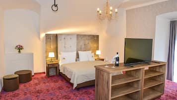 Habitación de hotel con una cama grande, un mueble de televisión de madera, un candelabro y una alfombra roja estampada.