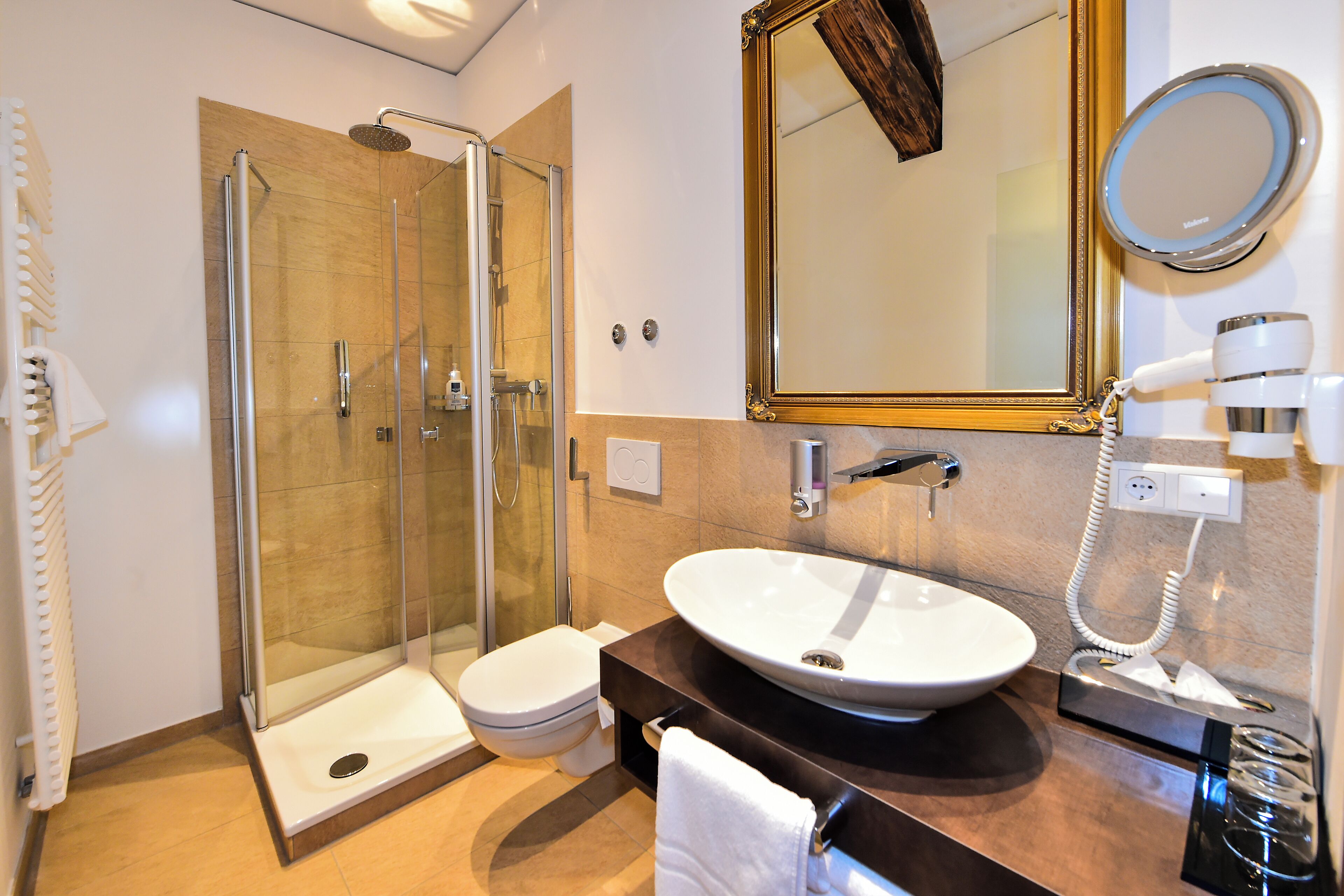Ein modernes Badezimmer mit einer Glaskabine zur Dusche, einem weißen Waschbecken und einem großen Spiegel.