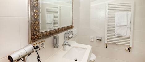 A bathroom with a large ornate mirror, a white sink, a hairdryer, and a towel rack.