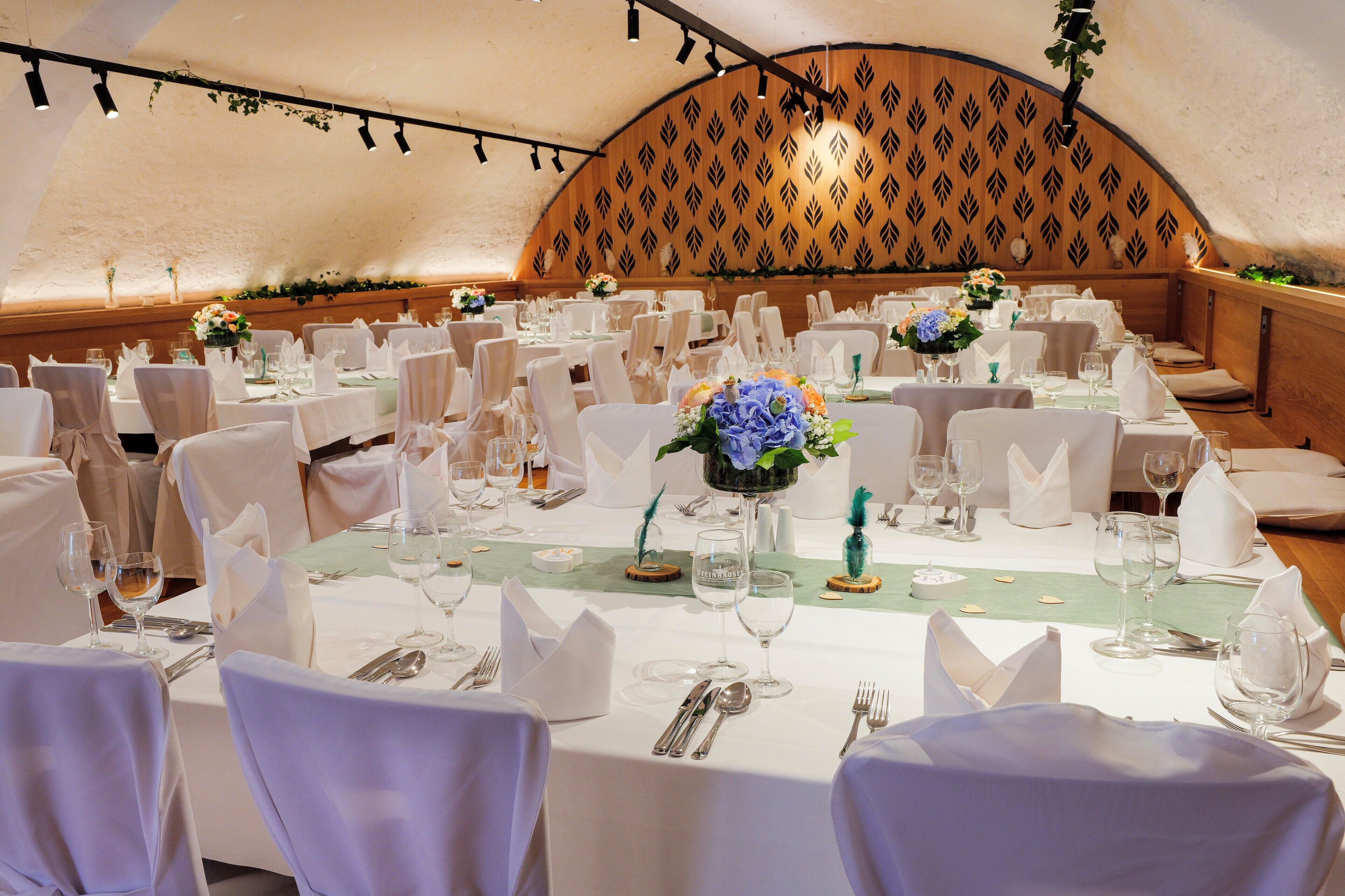 A banquet hall with round tables, white tablecloths, and floral centerpieces.