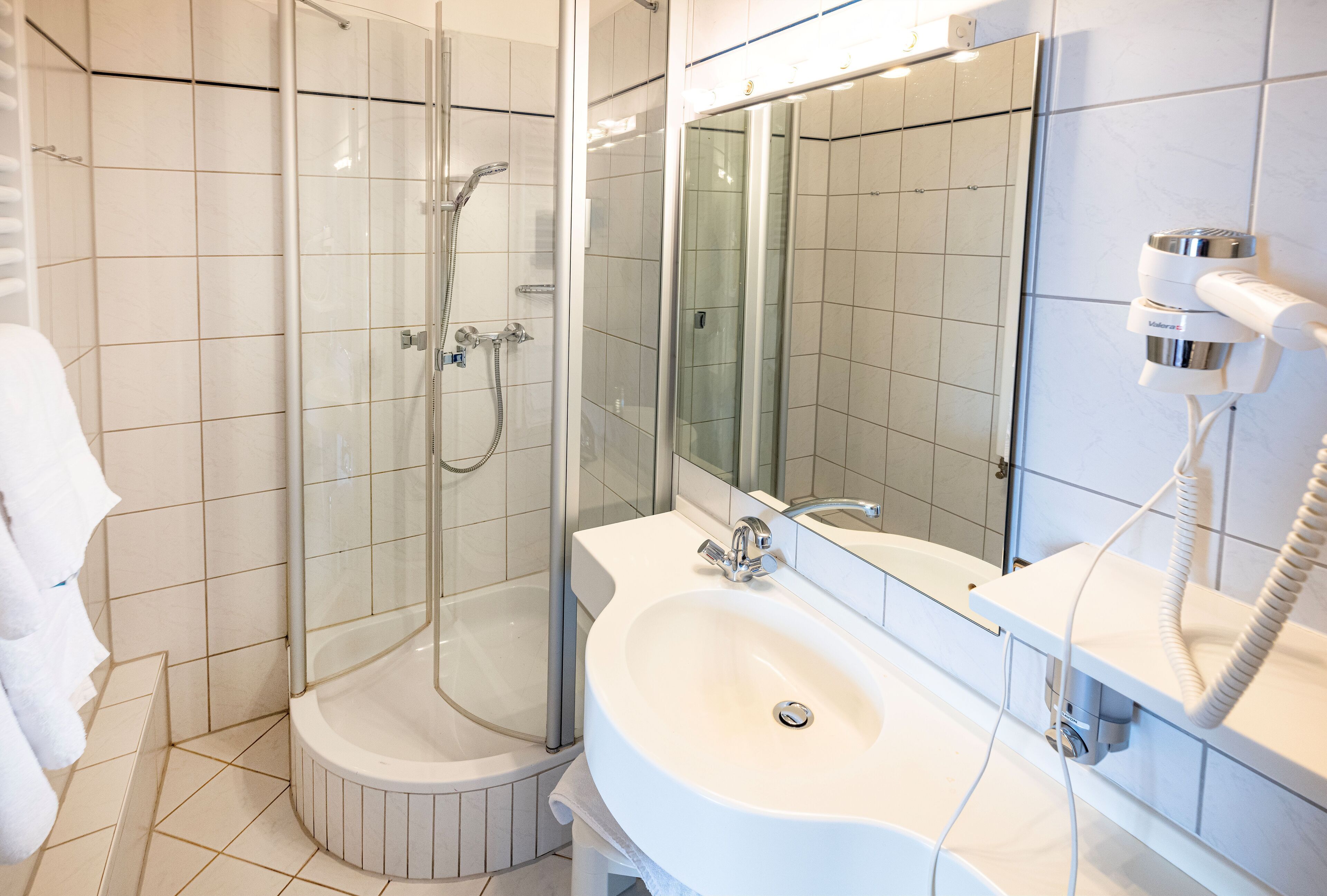A modern bathroom with a glass-enclosed shower, a white sink, and a hairdryer mounted on the wall.