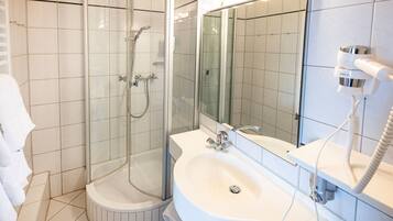 Une salle de bain moderne avec une douche à parois de verre, un lavabo blanc et un sèche-cheveux fixé au mur.