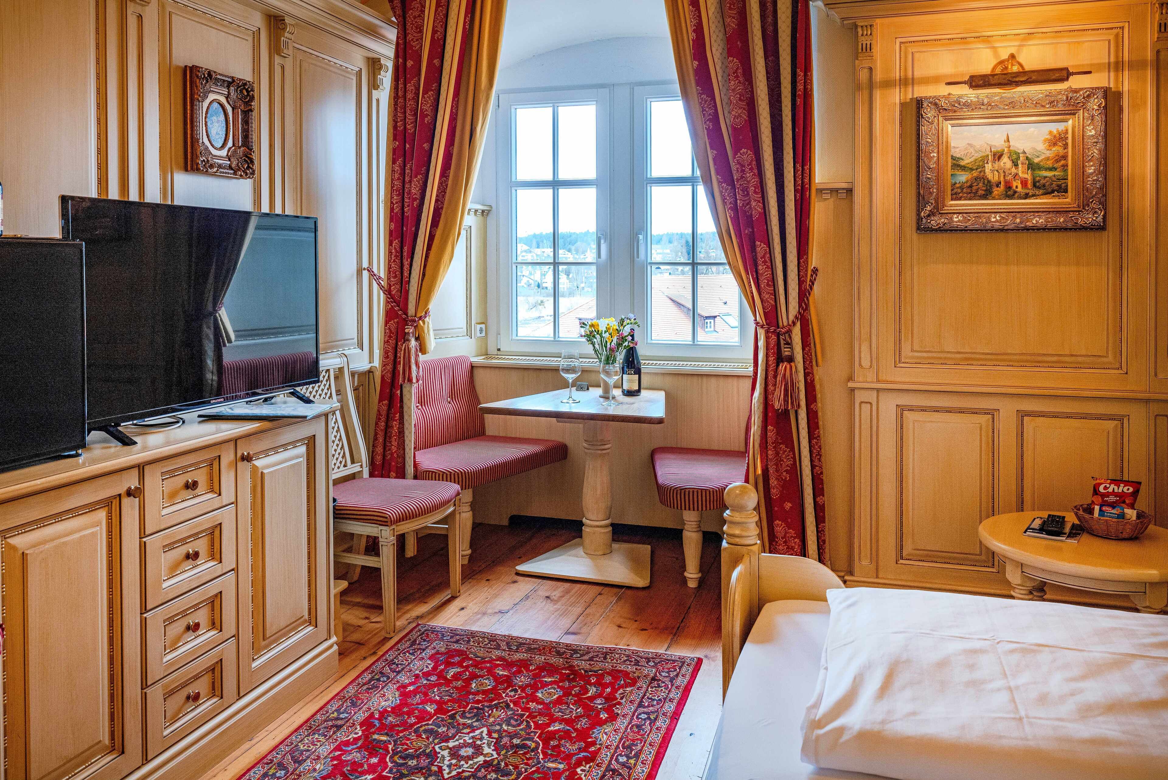 Ein Hotelzimmer mit Bett, Schreibtisch mit Stuhl, Fernseher und einem Fenster mit Vorhängen.