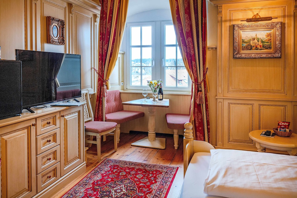 A hotel room with a bed, a desk with a chair, a television, and a window with curtains.
