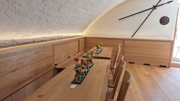 Een eetruimte met houten tafels en banken, een klok aan de muur en een raam voor natuurlijk licht.