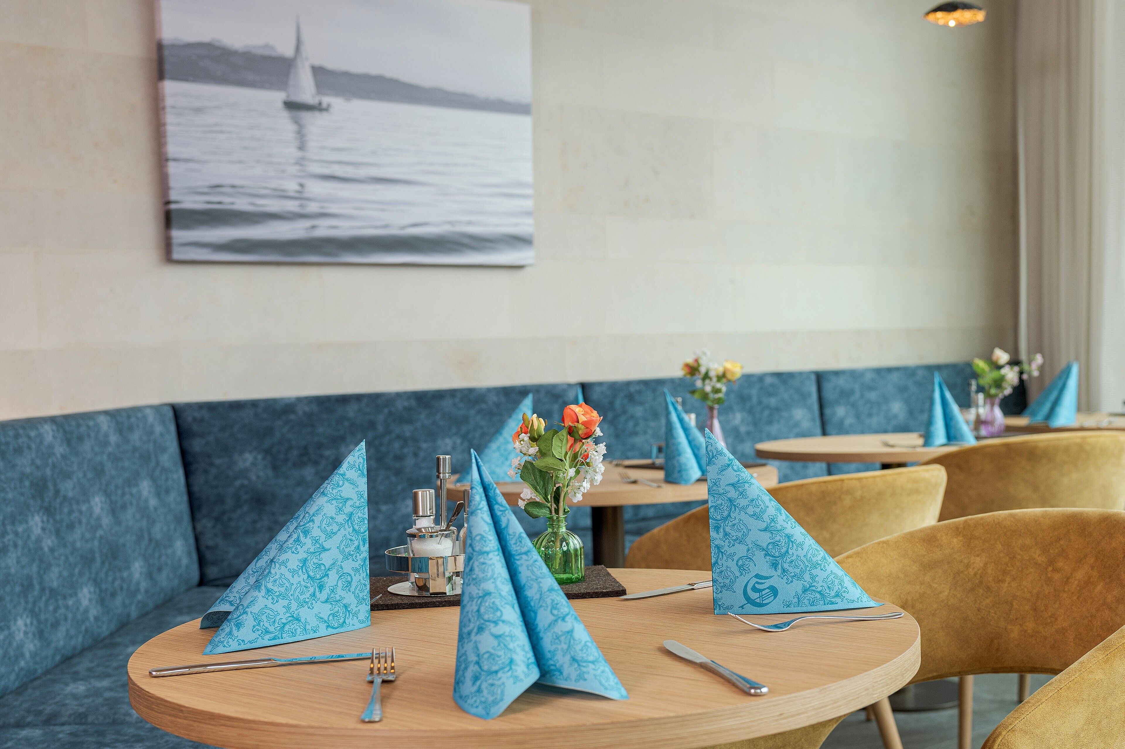 A restaurant interior with round tables, blue napkins, and a vase with flowers.