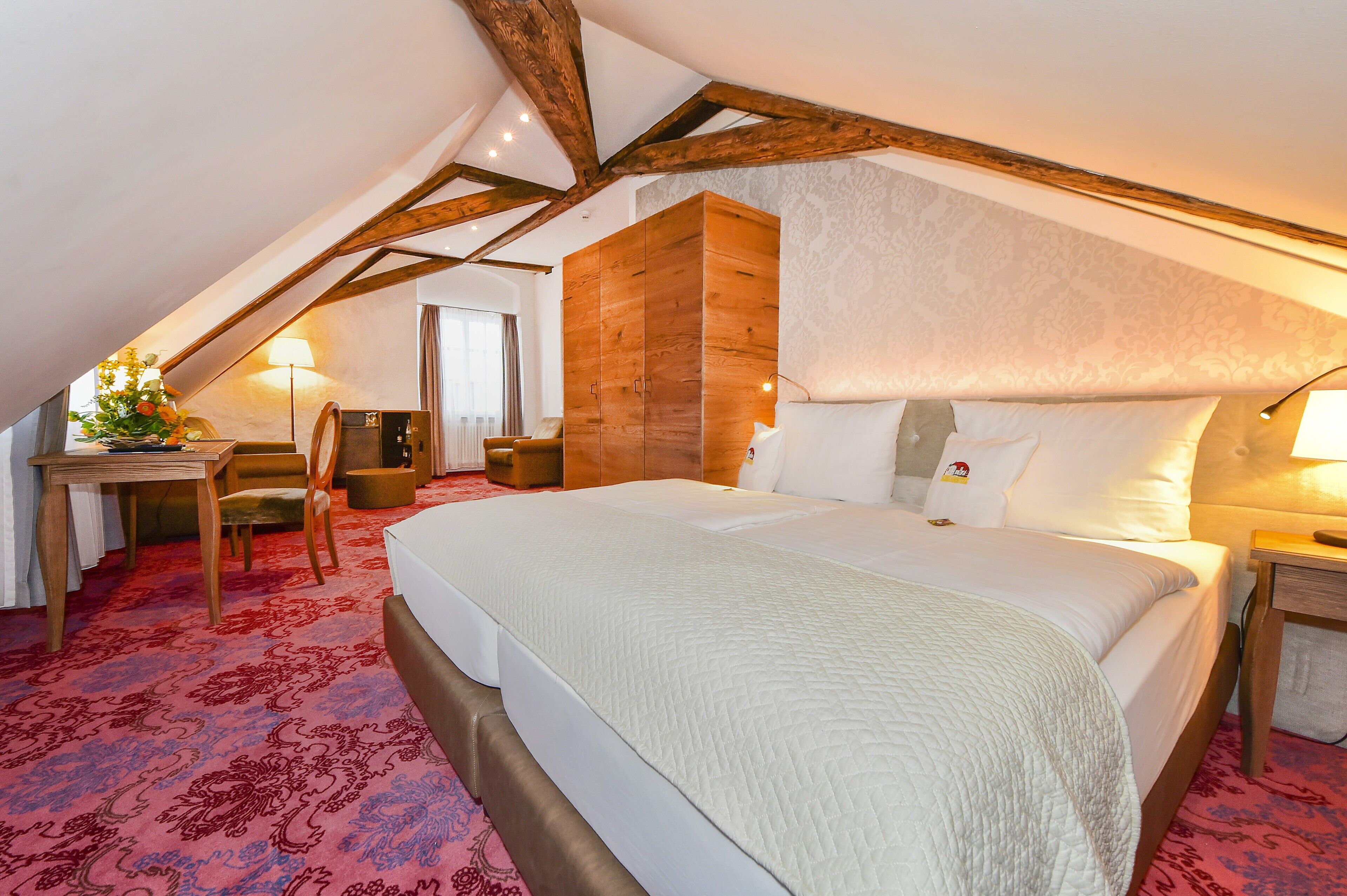 A bedroom with a large bed, wooden wardrobe, and a desk with a chair.