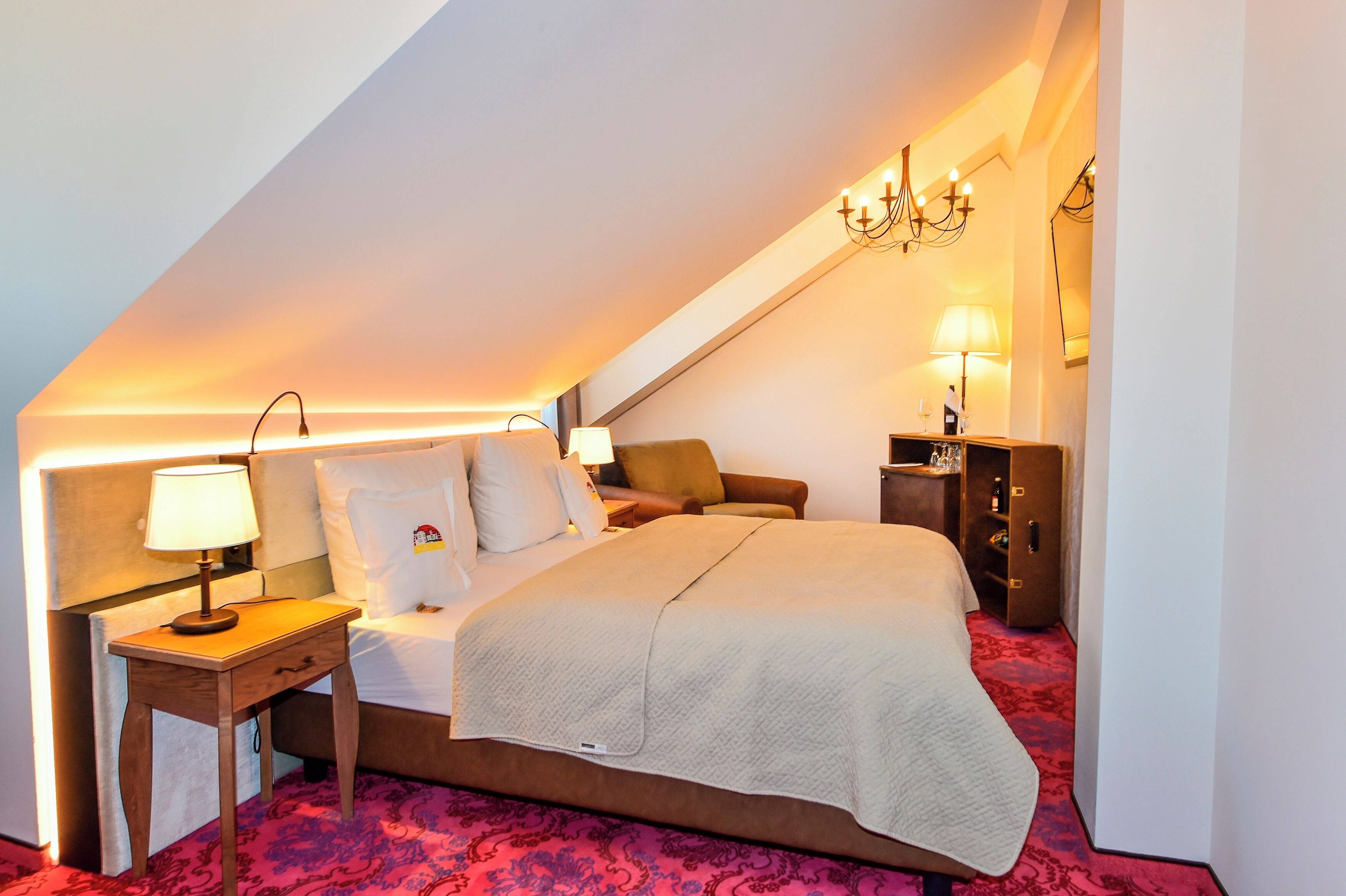 A hotel room with a bed, bedside table, lamp, and a nightstand.