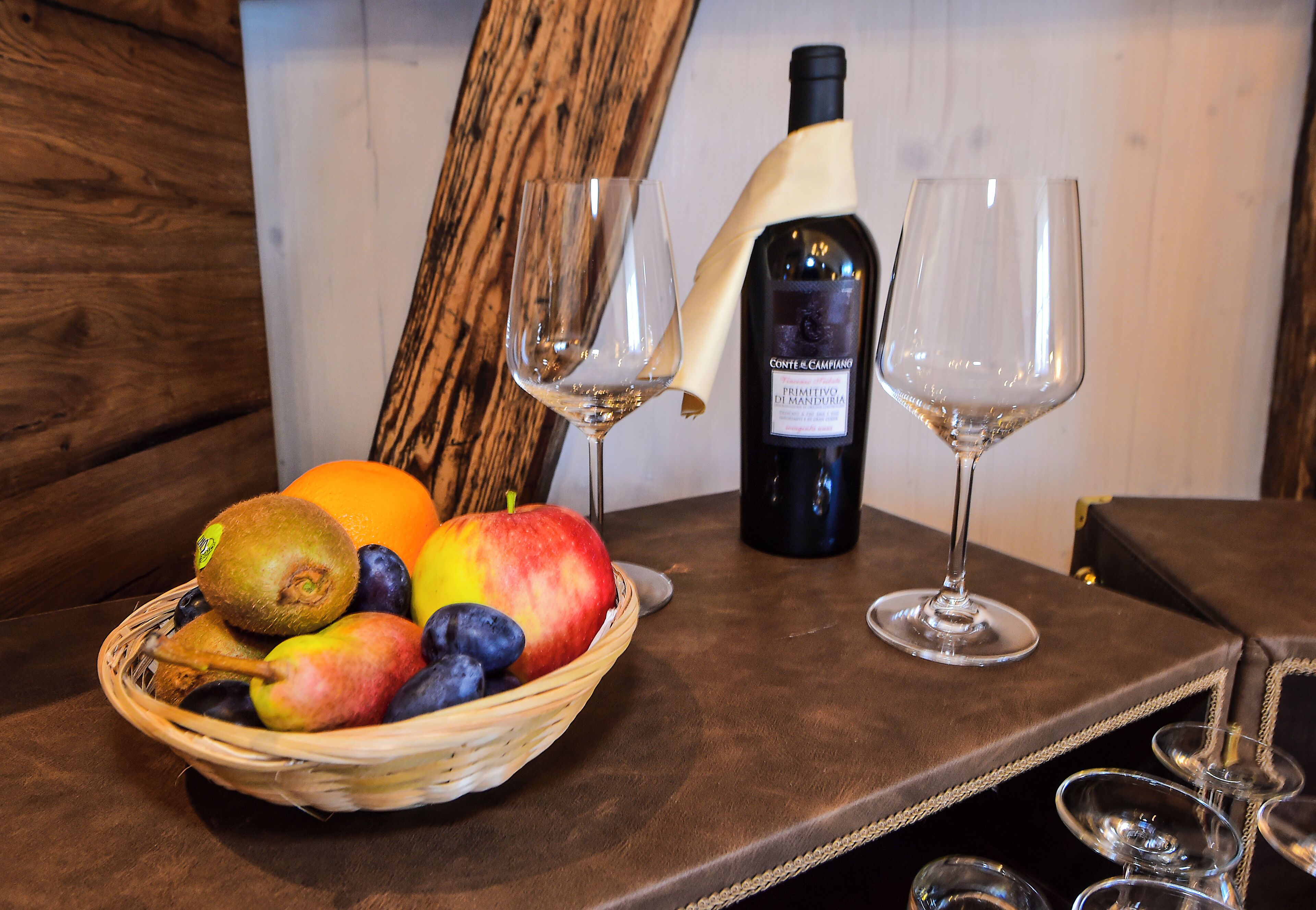 Una mesa con una botella de vino, dos copas y una cesta de frutas.