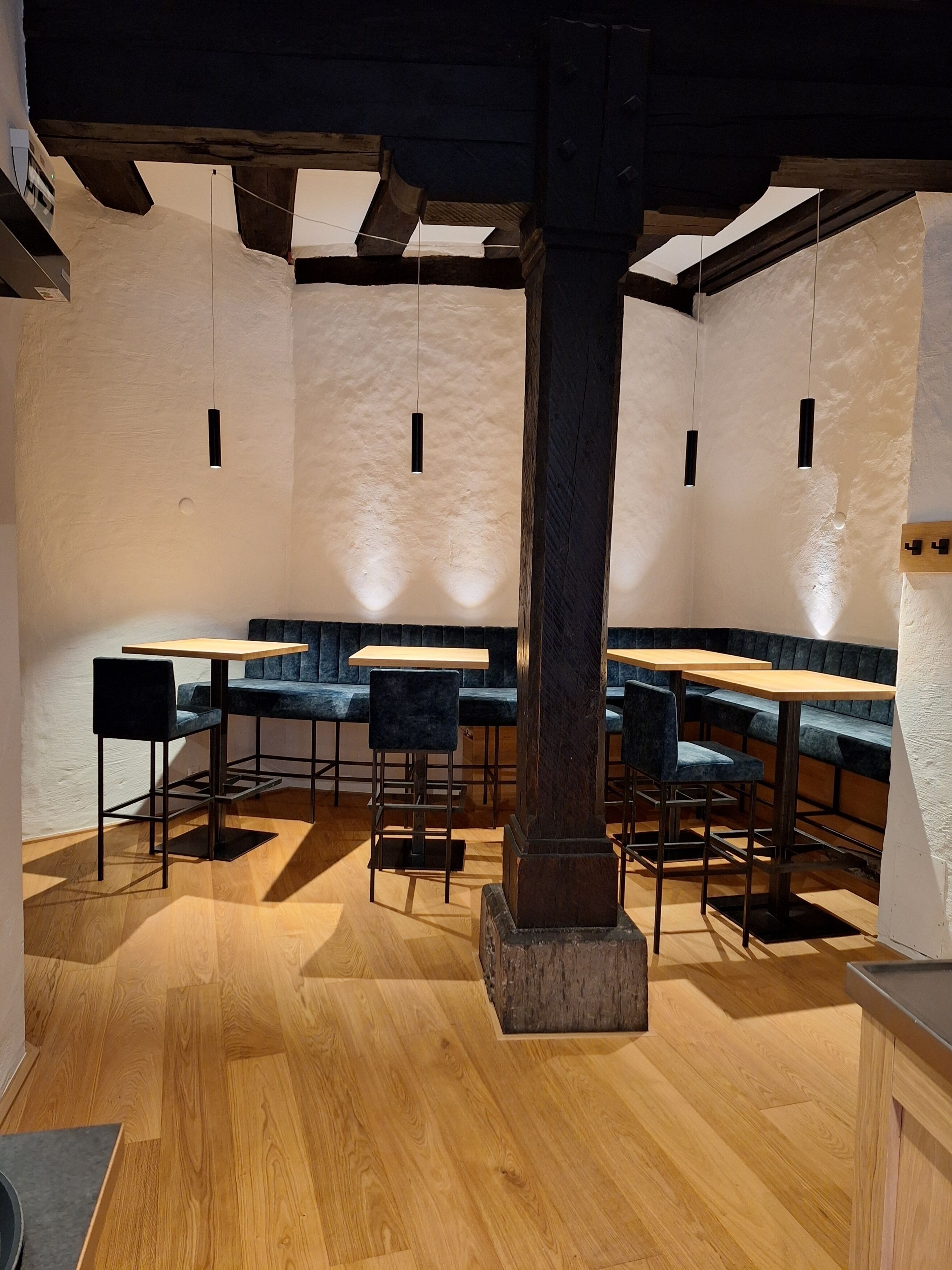 A modern interior with wooden flooring, dark blue upholstered seating, and hanging pendant lights.