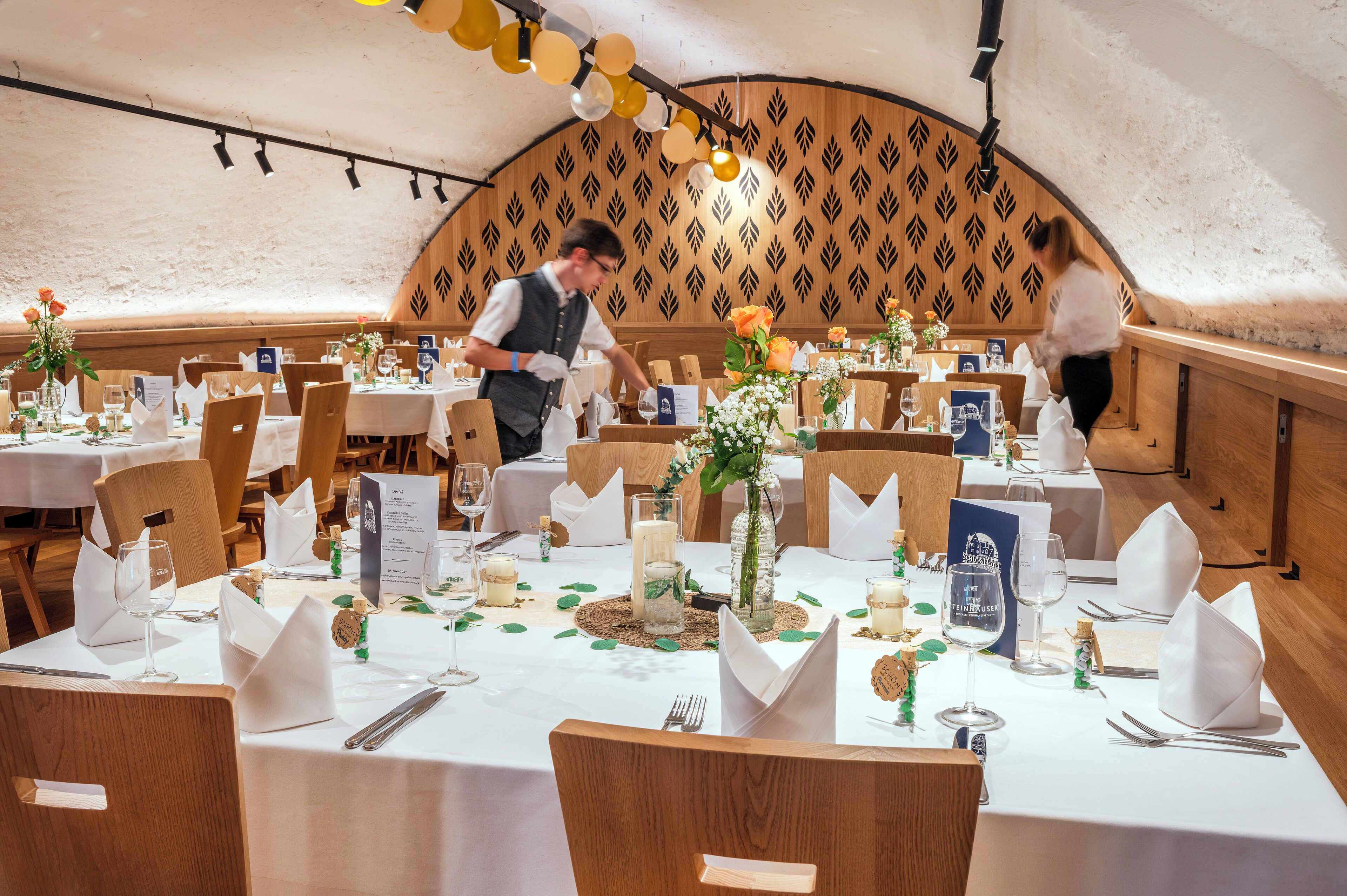 A restaurant with wooden tables, white tablecloths, and a patterned wall.