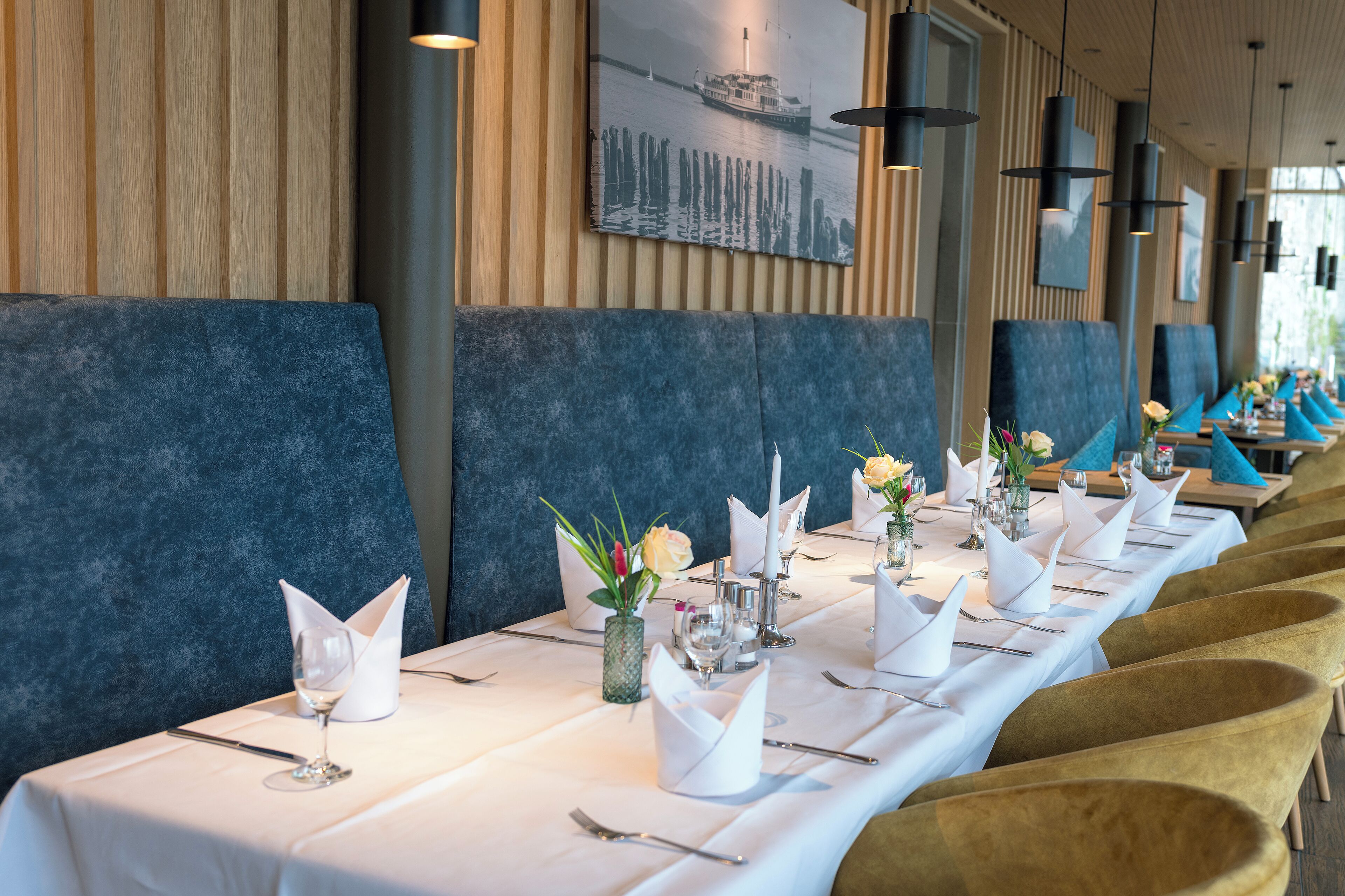 A long dining table set with white tablecloths, gold chairs, and neatly arranged cutlery.