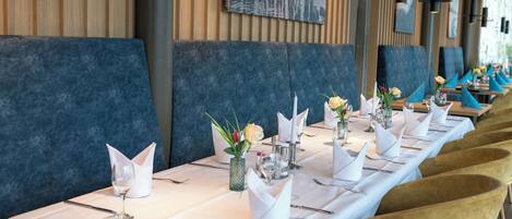 A long dining table set with white tablecloths, gold chairs, and neatly arranged cutlery.