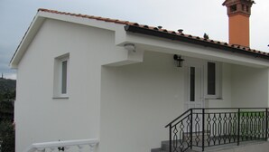 Un edificio bianco con tetto in tegole rosse, un piccolo balcone con ringhiere nere e una scalinata che conduce all'ingresso.