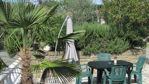 Un'area patio con pavimento in pietra, un tavolo con sedie, una pianta in vaso e un muro in pietra con vegetazione.