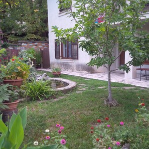 Ein Garten mit Teich, Kübelpflanzen und verschiedenen Blumen.