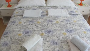 Un letto rifatto con lenzuola bianche, due cuscini e due asciugamani arrotolati su un copripiumino fantasia.