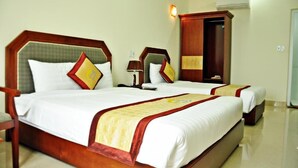 A hotel room with two beds, each with a wooden headboard, white bedding, and a red and yellow decorative border. There is a nightstand with a lamp and a mirror between the beds. - Hai Long Hotel (Hai Phong)