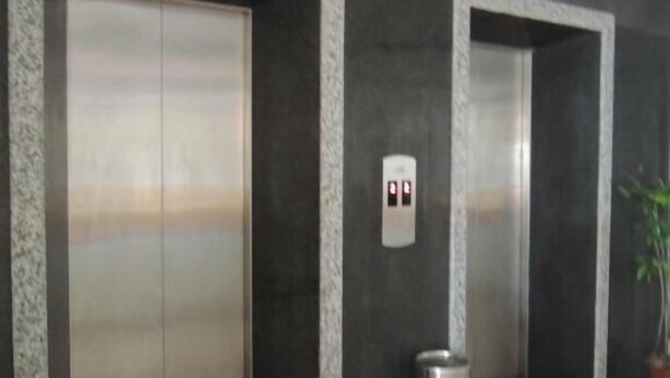 A modern elevator area with two elevators, a trash bin, and a potted plant. - Hai Long Hotel (Hai Phong)