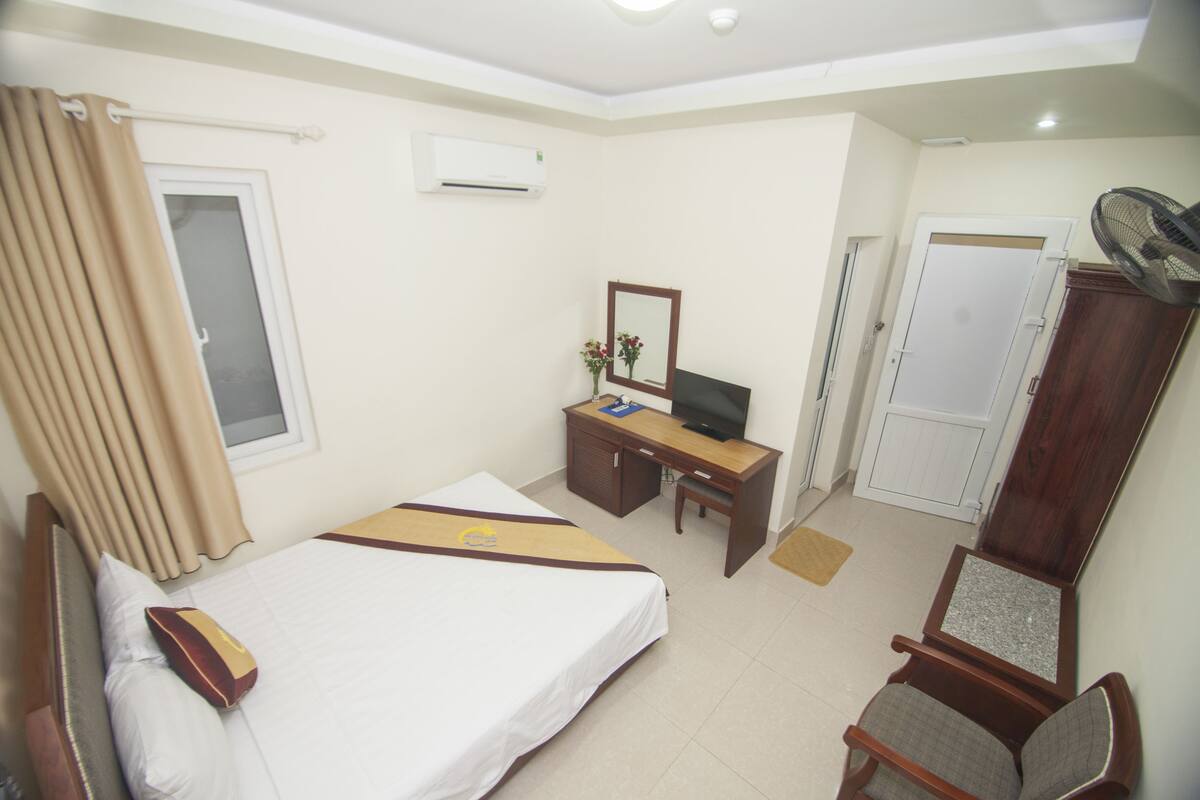 A hotel room with a bed, desk, chair, TV, and wardrobe.