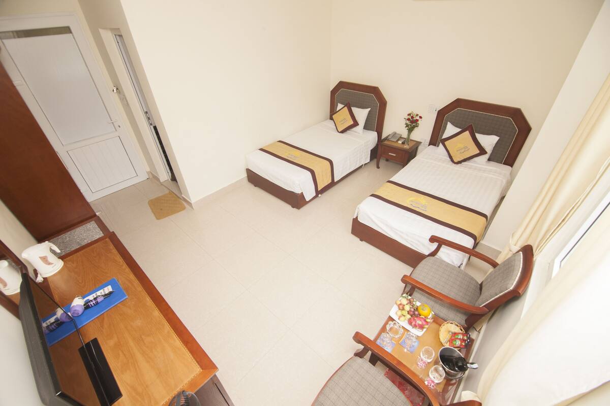 A hotel room with two single beds, a small table with a chair, and a desk with a chair.