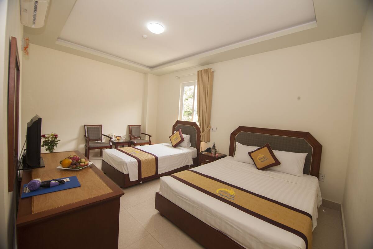 A hotel room with two beds, a desk, a chair, a TV, and a window with curtains.