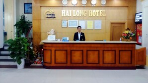 A reception desk at Hai Long Hotel with a receptionist, framed certificates, and a clock. - Hai Long Hotel (Hai Phong)